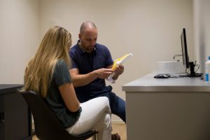 Sportfysiotherapeut Sven geeft aan de hand van een plastic kniemodel uitleg over de aandoening aan de klant